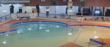 An indoor swimming pool with multiple lanes, a changing room area, and a seating area with chairs and tables.