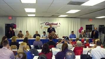 Un salón de conferencias con un escenario, asistentes sentados en mesas, y un cartel que dice "Cardinal".