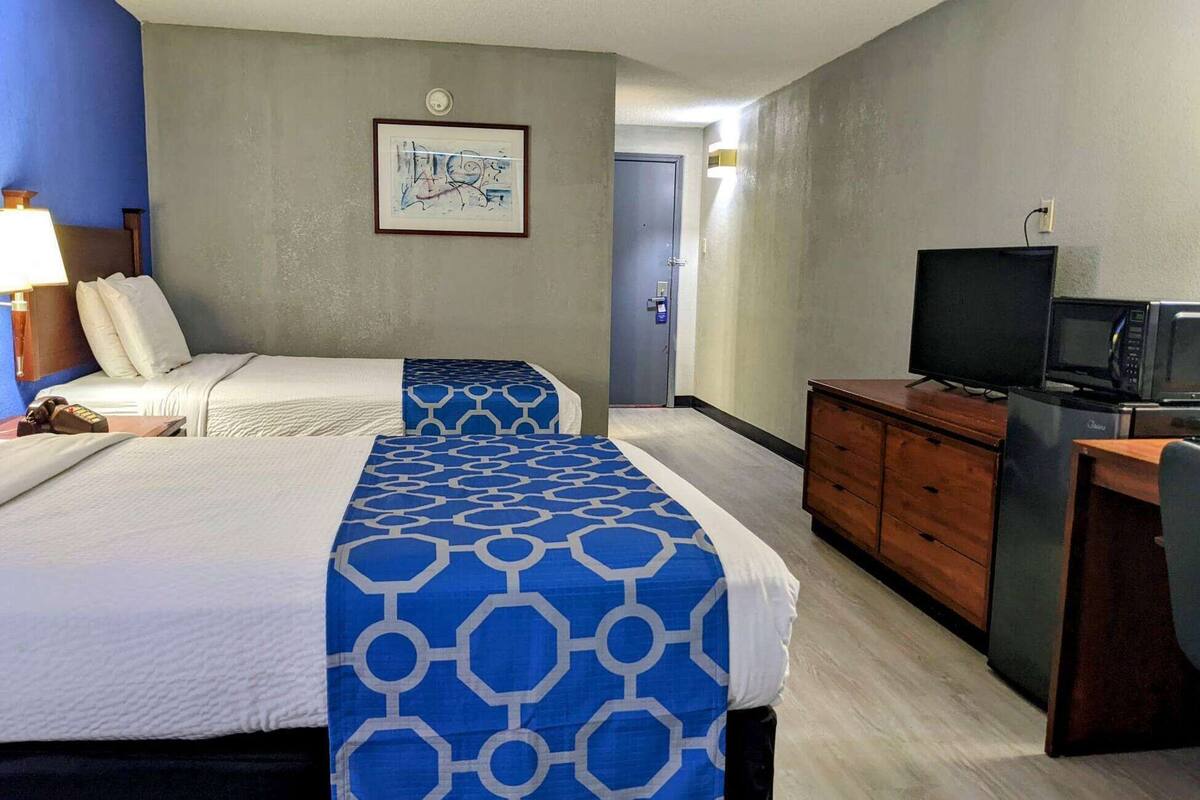 A hotel room with two beds, a television, a microwave, and a dresser.
