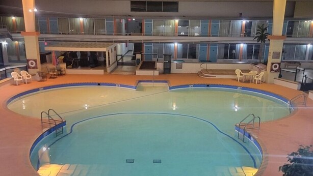 An indoor swimming pool with a tiled ceiling, multiple levels with windows, and seating areas around the pool. - Baymont by Wyndham Hannibal (Hannibal)