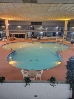 An indoor swimming pool with a tiled ceiling, multiple levels with windows, and seating areas around the pool. - Baymont by Wyndham Hannibal (Hannibal)