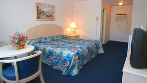 A hotel room with a bed, a table with a floral arrangement, a lamp, and a television. - Quarterdeck Motel (Wildwood)