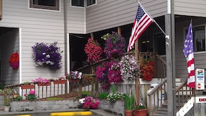 A building with a porch decorated with colorful flower planters and an American flag. - Tradewinds Motel (Rockaway Beach)
