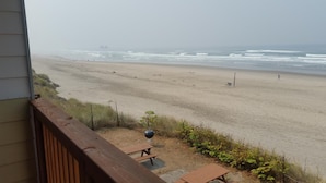 A beach view from a balcony with a wooden railing, a barbecue grill, and picnic tables. - Tradewinds Motel (Rockaway Beach)