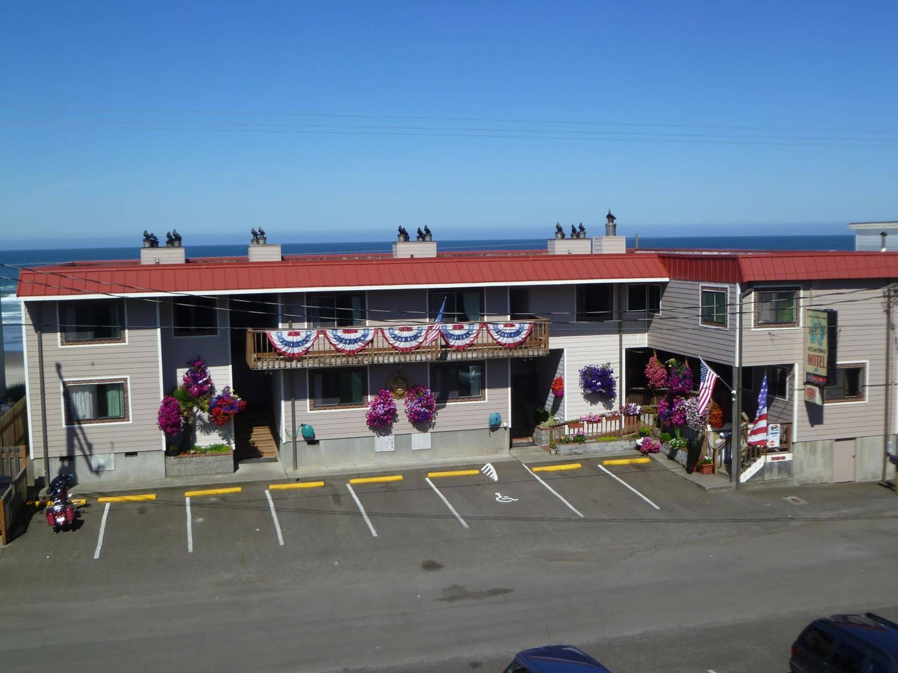 A motel with a red roof, a balcony with American flag decorations, and a parking lot with handicapped parking spaces.