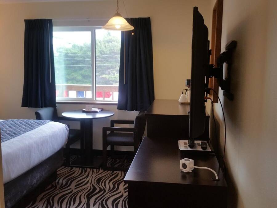 A hotel room with a bed, a desk with a computer, a chair, a small table, and a window with curtains.