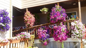 A porch with a wooden railing, hanging flower baskets, and a stone wall. - Tradewinds Motel (Rockaway Beach)