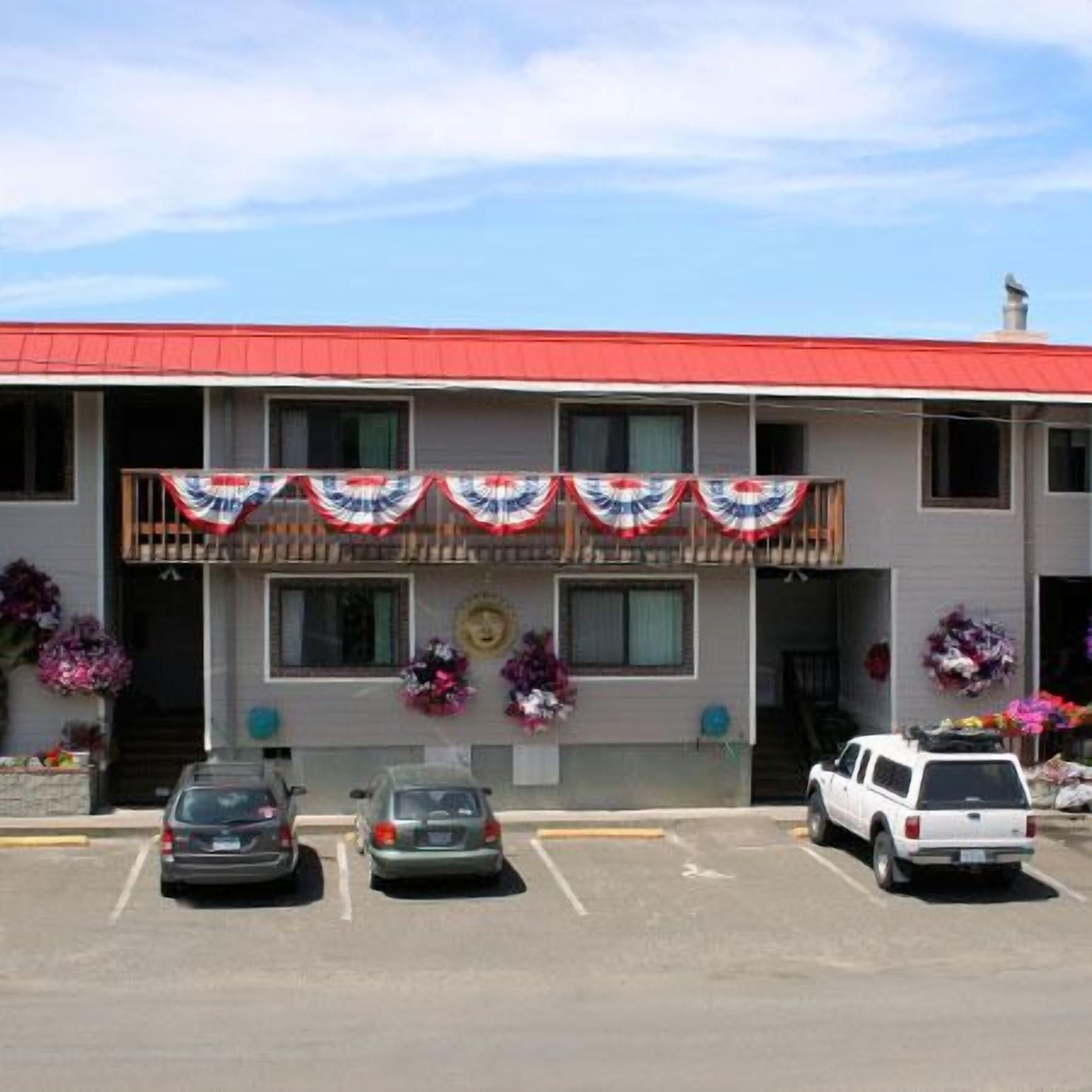 A motel with a red roof, a covered front porch, and a parking lot with several cars.