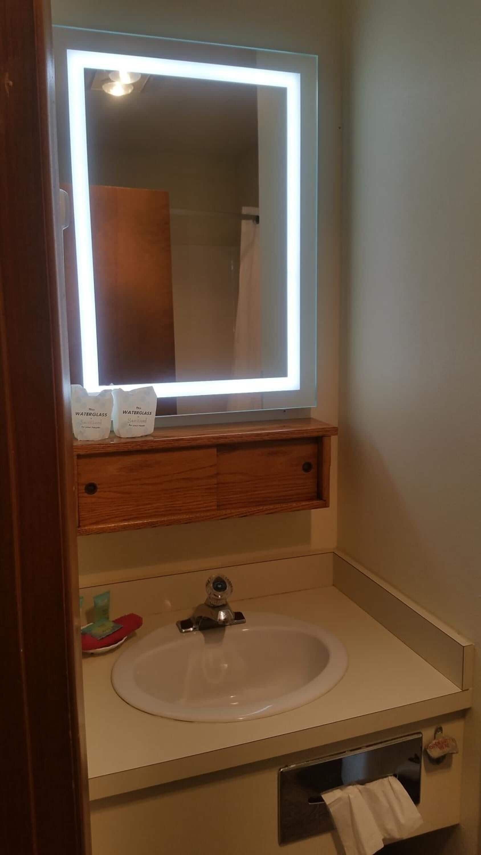 A bathroom with a white sink, a mirror with a light, and a wooden vanity.