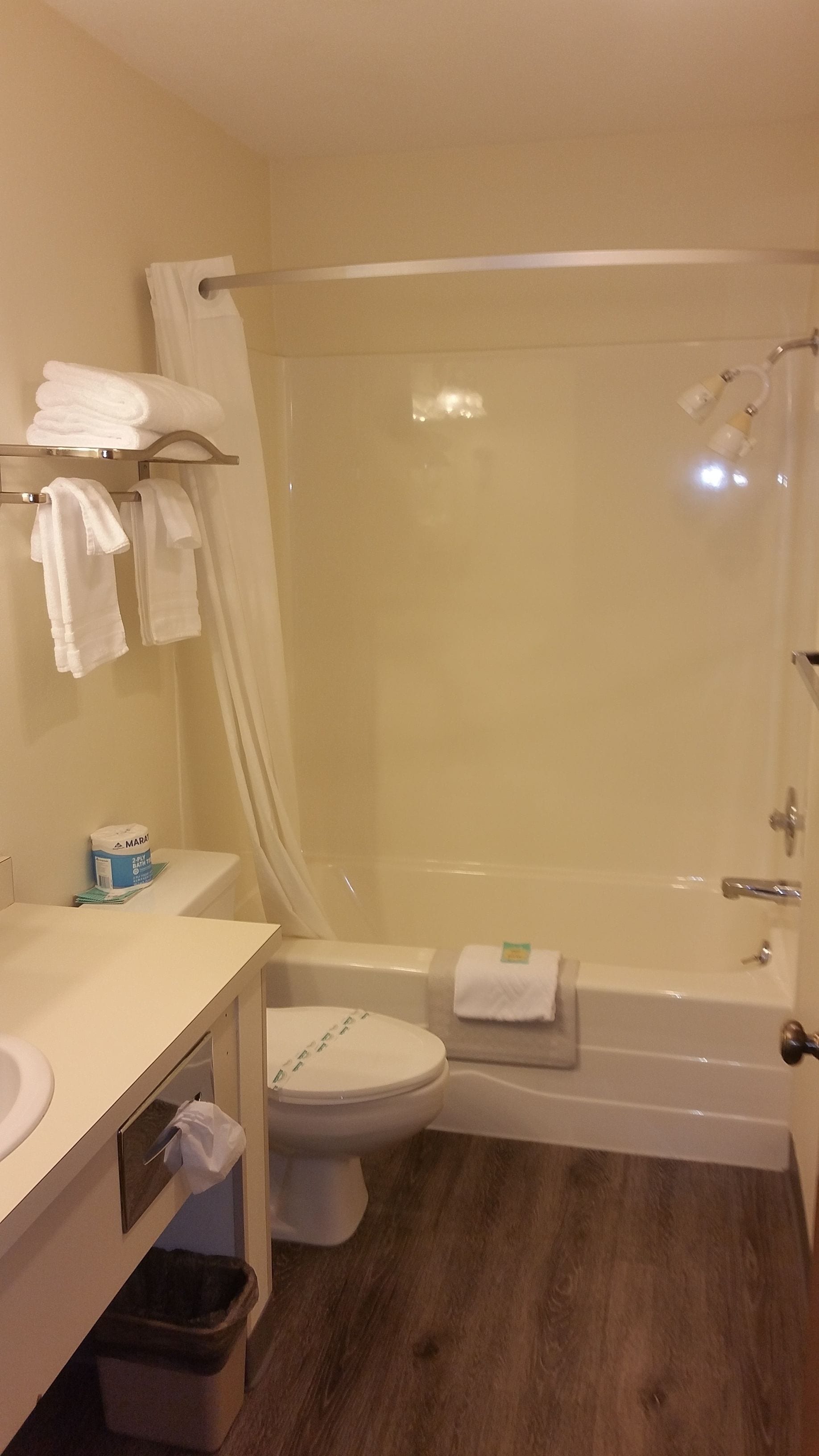 A bathroom with a toilet, sink, and bathtub. There are towels on the wall and a trash bin.