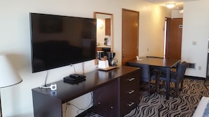 A hotel room with a flat-screen TV, a coffee maker, a desk with a chair, and a patterned carpet. - Tradewinds Motel (Rockaway Beach)
