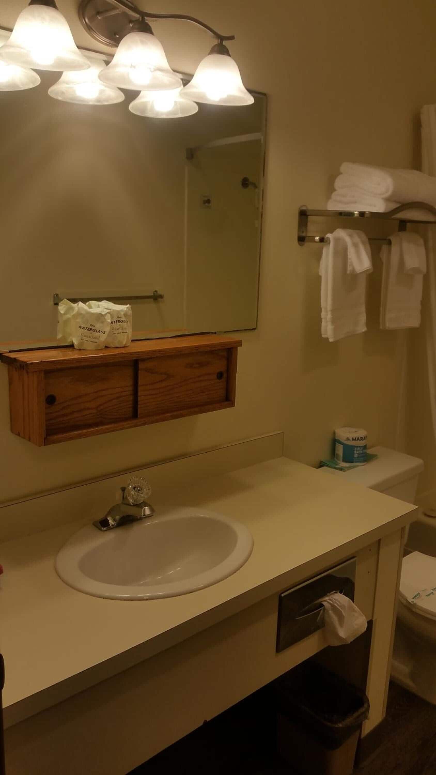 Un baño con lavamanos blanco, espejo, toallero y mueble de madera.