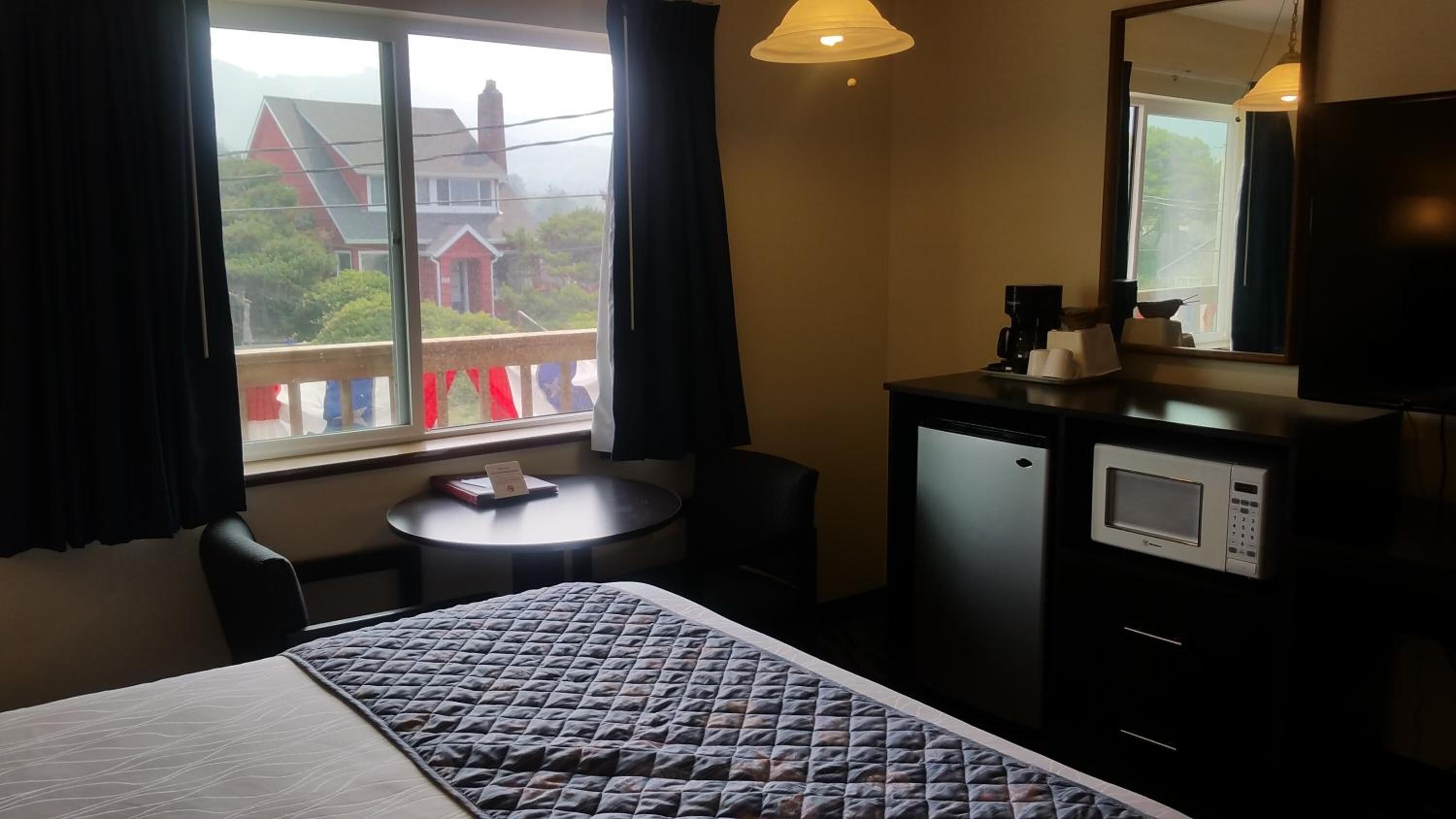 A hotel room with a bed, a small desk, a microwave, and a window with curtains.