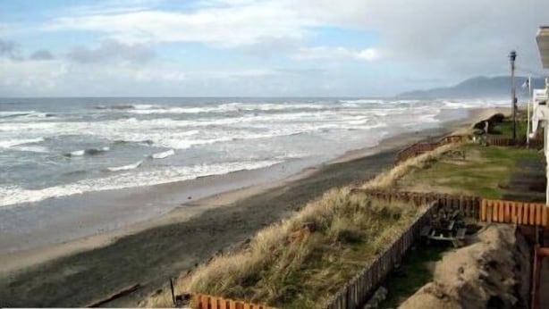 A coastal view with a beach, grassy areas, and a structure on the right. - Tradewinds Motel (Rockaway Beach)