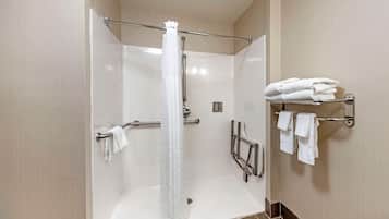 Un espace douche moderne doté d’une porte en verre, d’un pommeau de douche, d’une barre d’appui et d’un porte-serviettes avec des serviettes pliées.