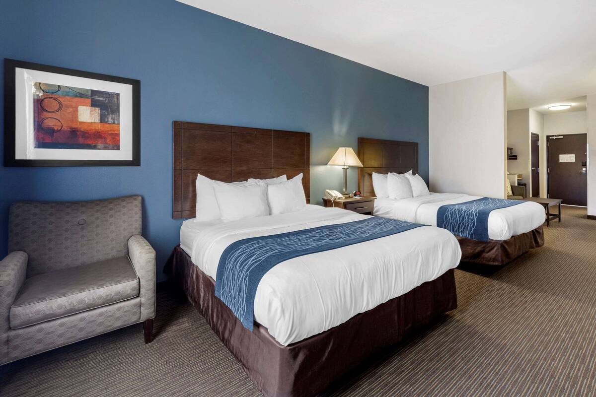 A hotel room with two beds, a sofa, a framed picture on the wall, and a lamp on the nightstand.