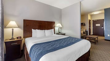 Habitació d'hotel amb un llit gran, dues taules de nit amb làmpades, una taula petita i una porta que dona a una altra habitació.