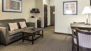 A hotel room with a sofa, a small table, a chair, a microwave, a refrigerator, and framed pictures on the walls. - Comfort Inn & Suites Oklahoma City West - I-40 (Oklahoma City)