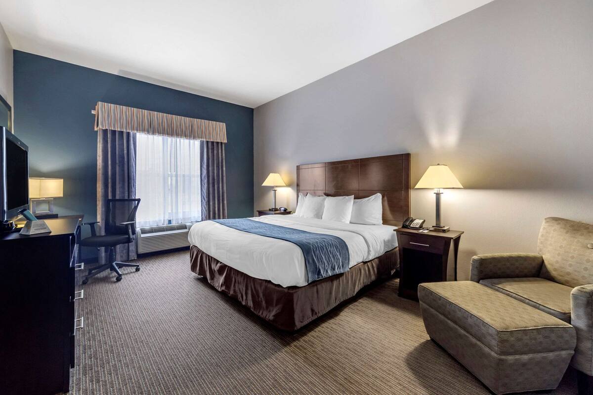 A hotel room with a large bed, two bedside lamps, a desk with a chair, and a sofa.