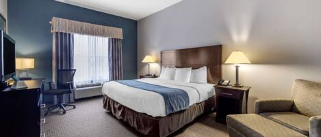 A hotel room with a large bed, two bedside lamps, a desk with a chair, and a sofa.