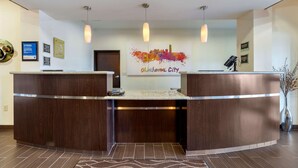 A reception area with a wooden reception desk, a cityscape artwork, and a sign indicating a check-in counter. - Comfort Inn & Suites Oklahoma City West - I-40 (Oklahoma City)