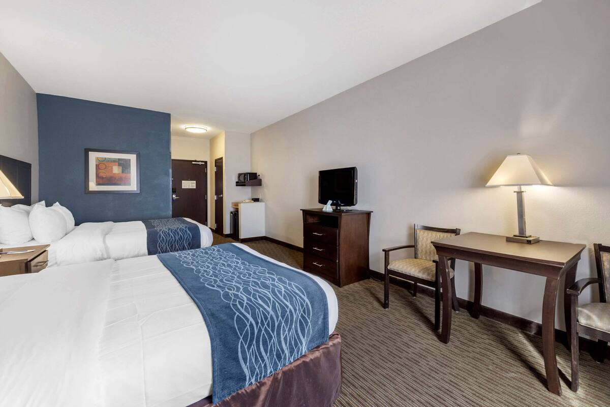 A hotel room with two beds, a desk, a chair, a television, and a lamp.