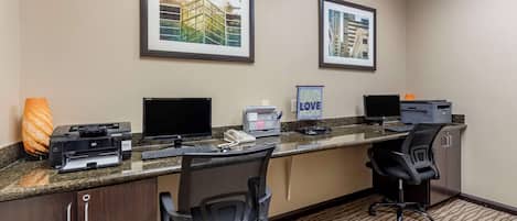 A hotel reception desk with two computer monitors, a printer, a telephone, and framed pictures on the wall.