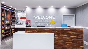 Un comptoir d’accueil d’hôtel avec une pancarte de bienvenue, un mur en bois et des étagères remplies de collations.
