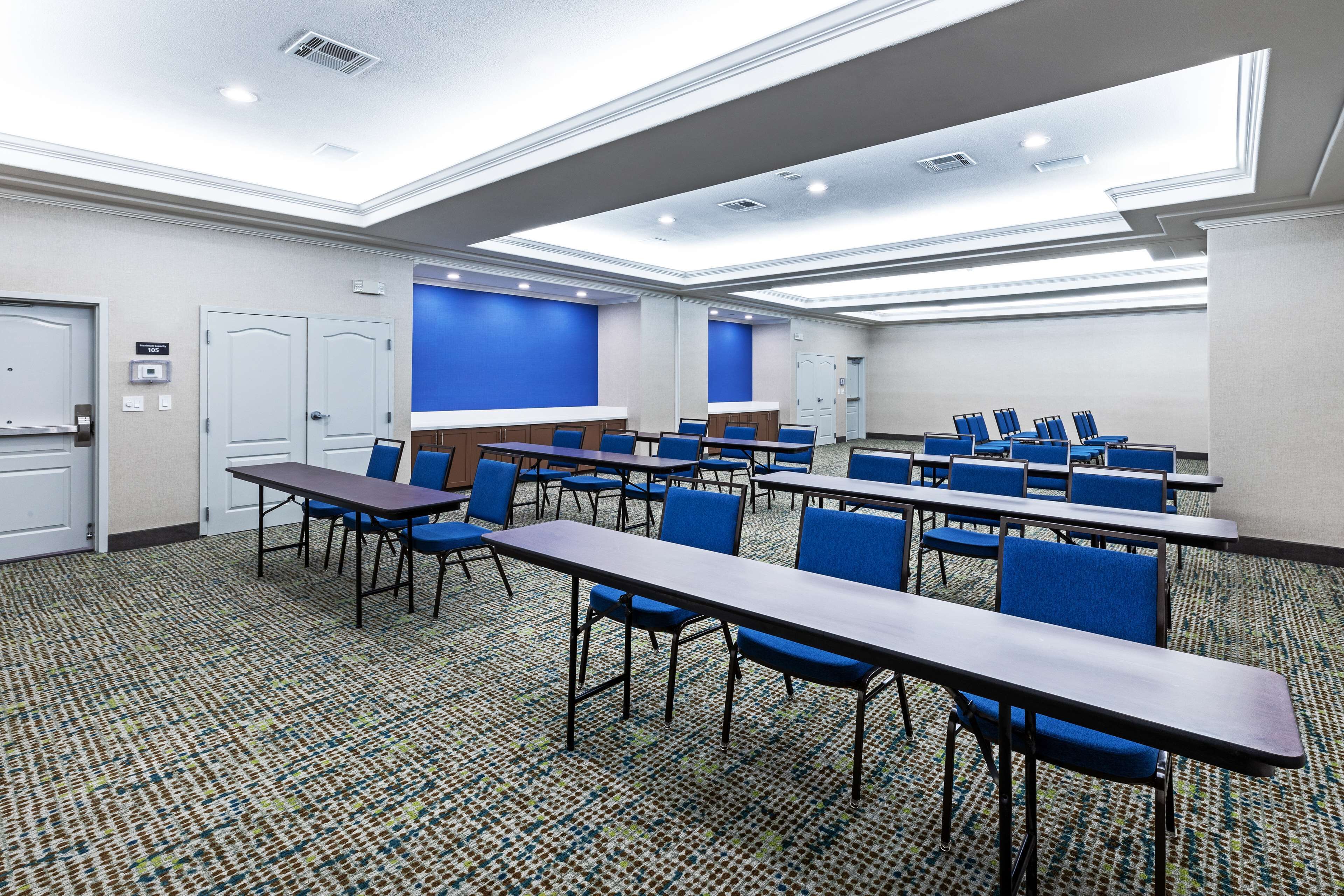 A conference room with multiple tables and chairs, carpeted flooring, and a blue accent wall.