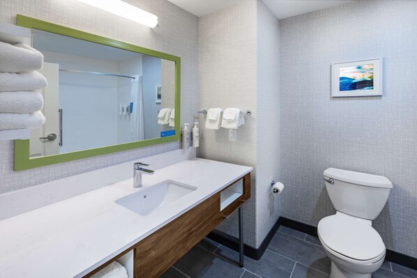 A modern bathroom with a white sink, green-framed mirror, white towels, and a toilet.