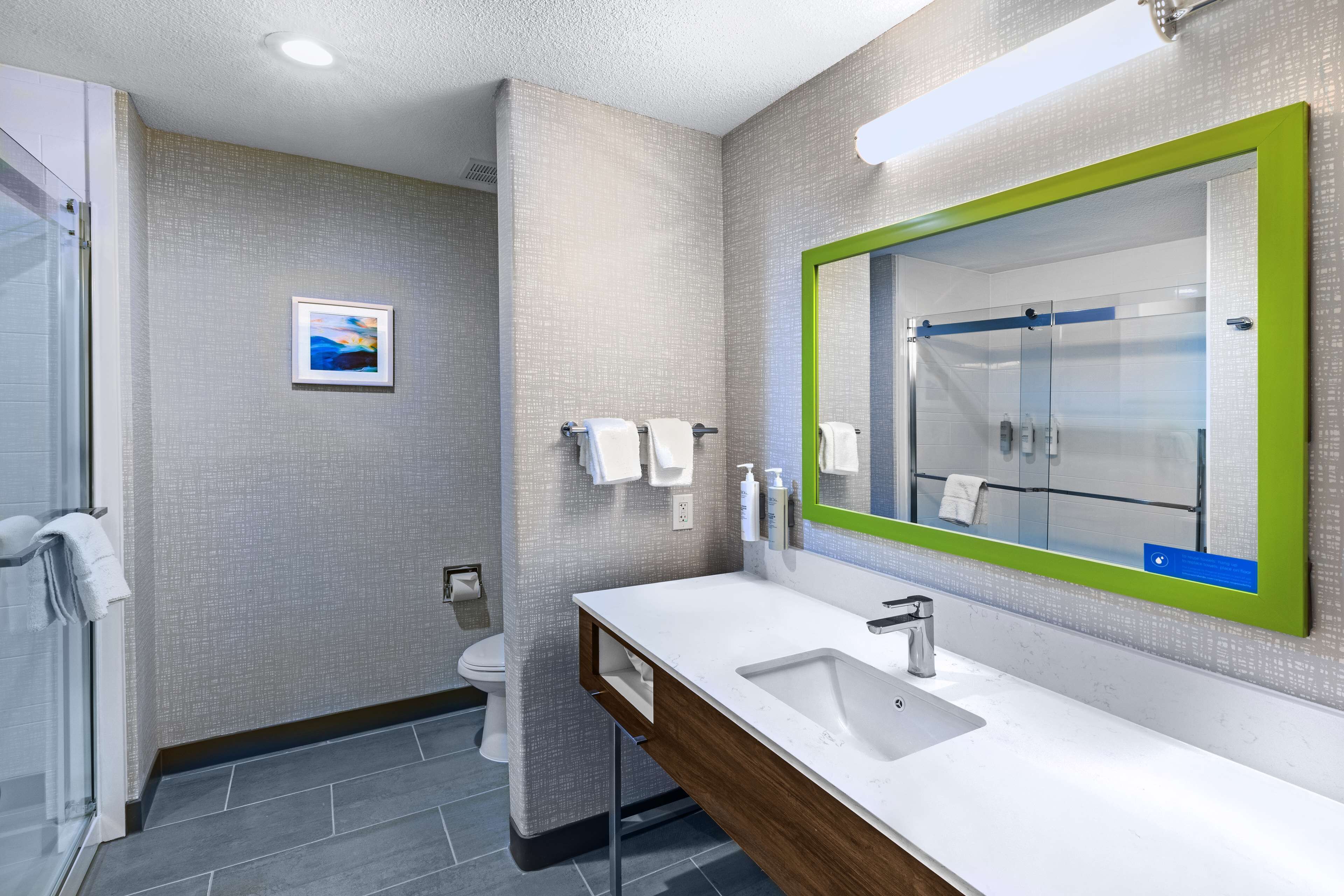 Un baño moderno con un espejo grande, lavamanos blanco y cabina de ducha de vidrio.