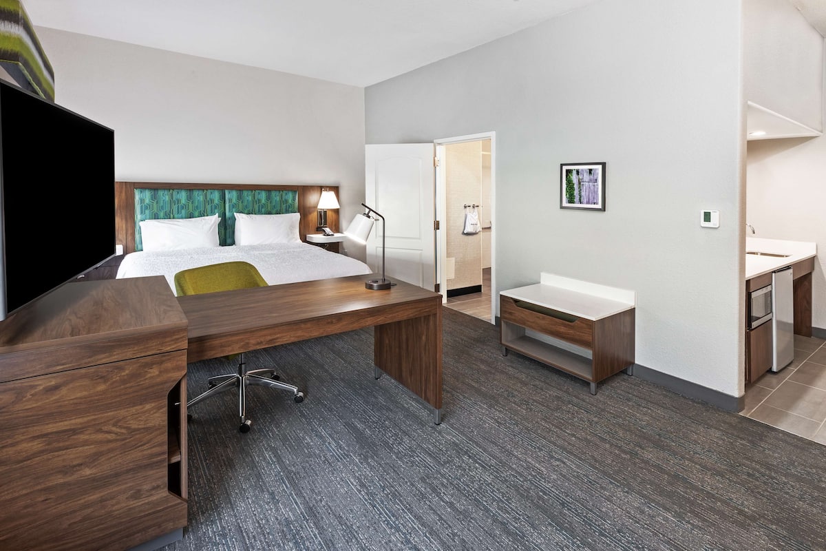 A hotel room with a bed, desk, chair, and a small kitchenette.