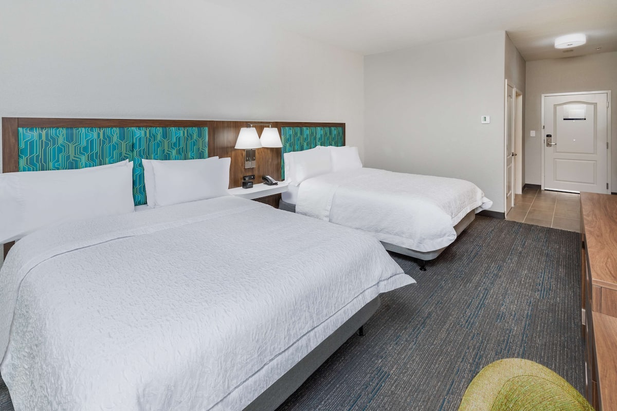 A hotel room with two beds, a nightstand with lamps, a door, and a carpeted floor.