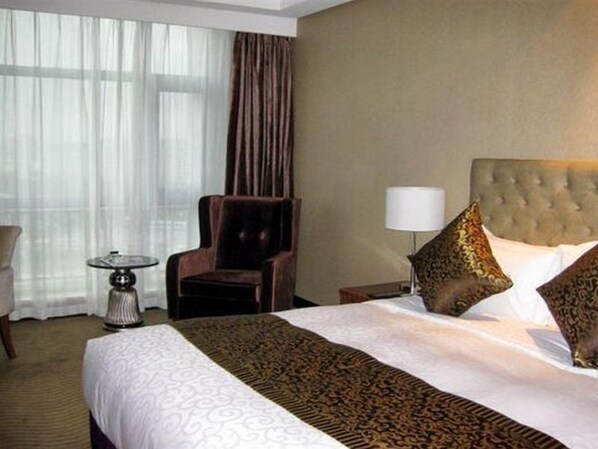 Une chambre d’hôtel avec un grand lit, une chaise, une lampe et une fenêtre avec des rideaux.