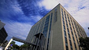A modern building with a prominent logo on the facade, multiple windows, and a clear sky with clouds. - Intl Talent City Hotel (Shanghai)