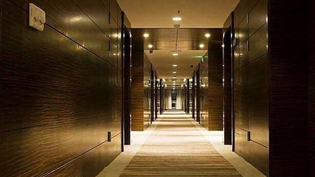 A long, narrow hallway with wooden walls and a carpeted floor, leading to a bright area at the end. - Intl Talent City Hotel (Shanghai)