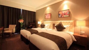 A hotel room with two beds, a sitting area with a chair, a desk, and a lamp. - Intl Talent City Hotel (Shanghai)