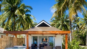 Une terrasse en bois avec un jacuzzi, des sièges d’extérieur et une vue sur les palmiers.