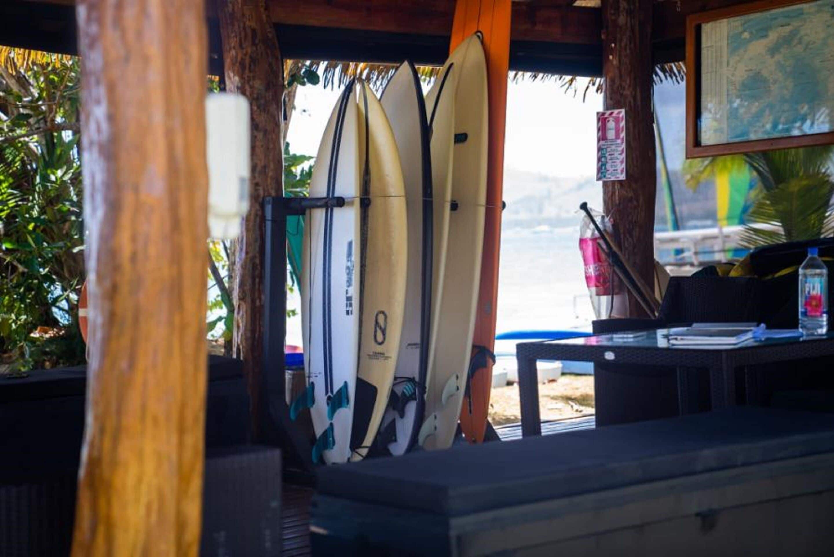 A covered area with surfboards leaning against a wall, a map on the wall, and a table with a bottle and a notebook.