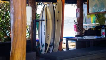 A covered area with surfboards leaning against a wall, a map on the wall, and a table with a bottle and a notebook.