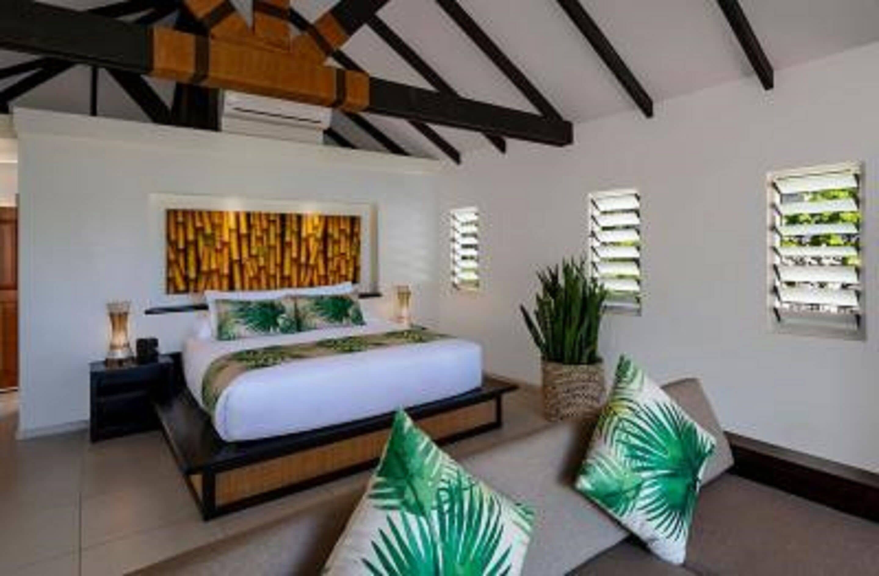 A modern bedroom with a bed, bedside tables, a wall-mounted light fixture, and a large plant.