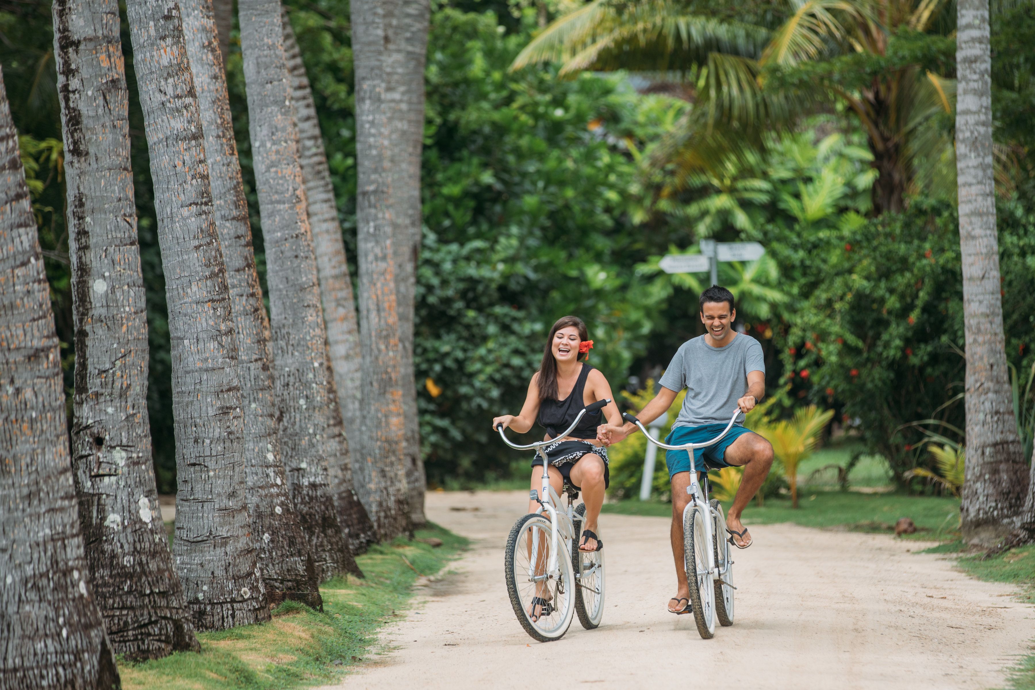 Dos personas paseando en bicicleta por un sendero de tierra rodeado de árboles.