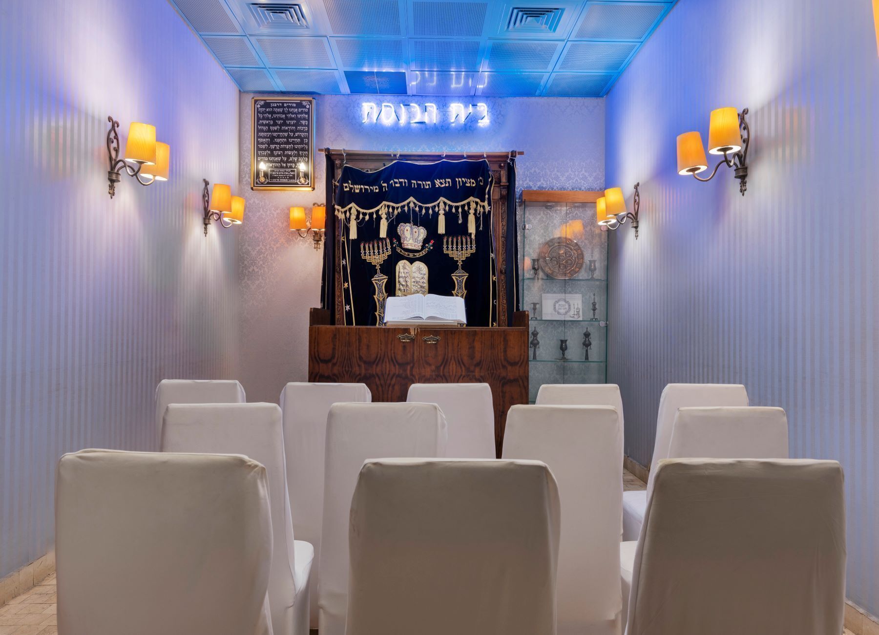 Innenansicht einer Synagoge mit Reihen von Stühlen, einer Thora-Rolle und einer brennenden Menora.