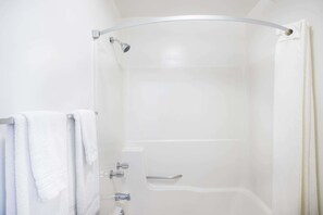 A modern shower with a curved glass door, a handheld showerhead, and a control panel with multiple knobs. - Lake George, Ny Travelodge (Lake George)