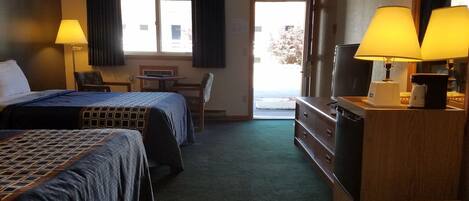 A hotel room with two beds, a desk, a chair, a dresser, and a television.