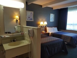 A hotel room with a large mirror, a sink, two beds with dark bedding, two bedside lamps, and a window with curtains. - Lake George, Ny Travelodge (Lake George)