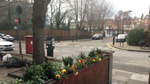 A street view with a wooden planter box containing flowers, a red post box, and a pay by machine. - Simply Rooms & Suites (London)