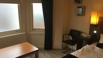 A hotel room with a bed, a desk, a chair, a nightstand, and a window with curtains.