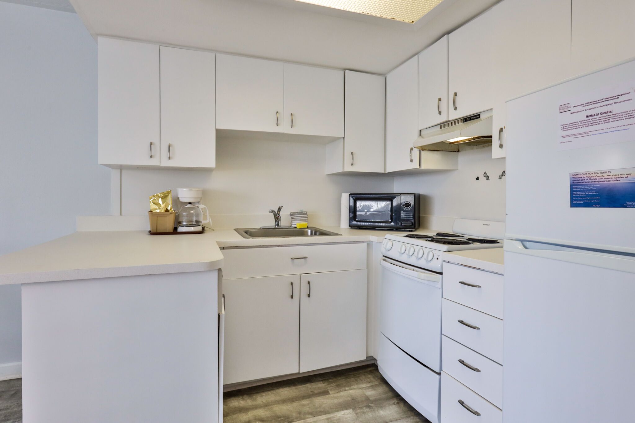 A compact kitchen with white cabinets, a microwave, a stove, and a refrigerator.