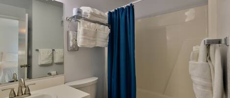 A bathroom with a sink, toilet, and shower. There are towels hanging on a rack.